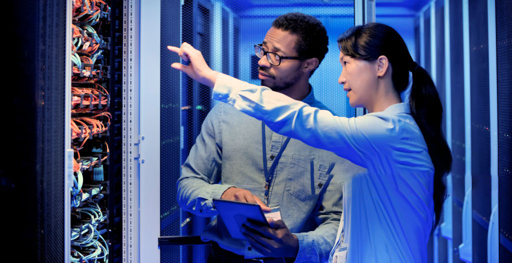 Male and female IT engineers checking servers in server room with help of tablet.