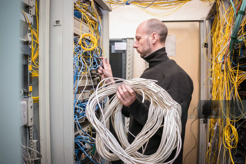 The signalman holds in his hands many wires wound in a ring. The specialist works in the server room of the data center. A man switches many cables in a server rack.
