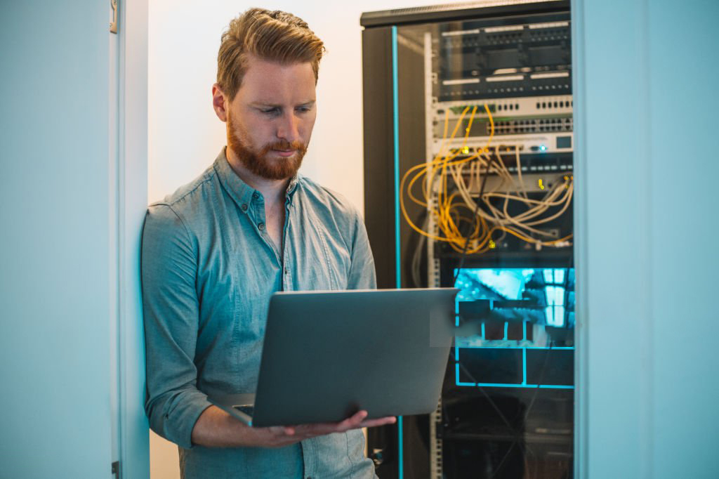 Male Caucasian IT technician using laptop in server room