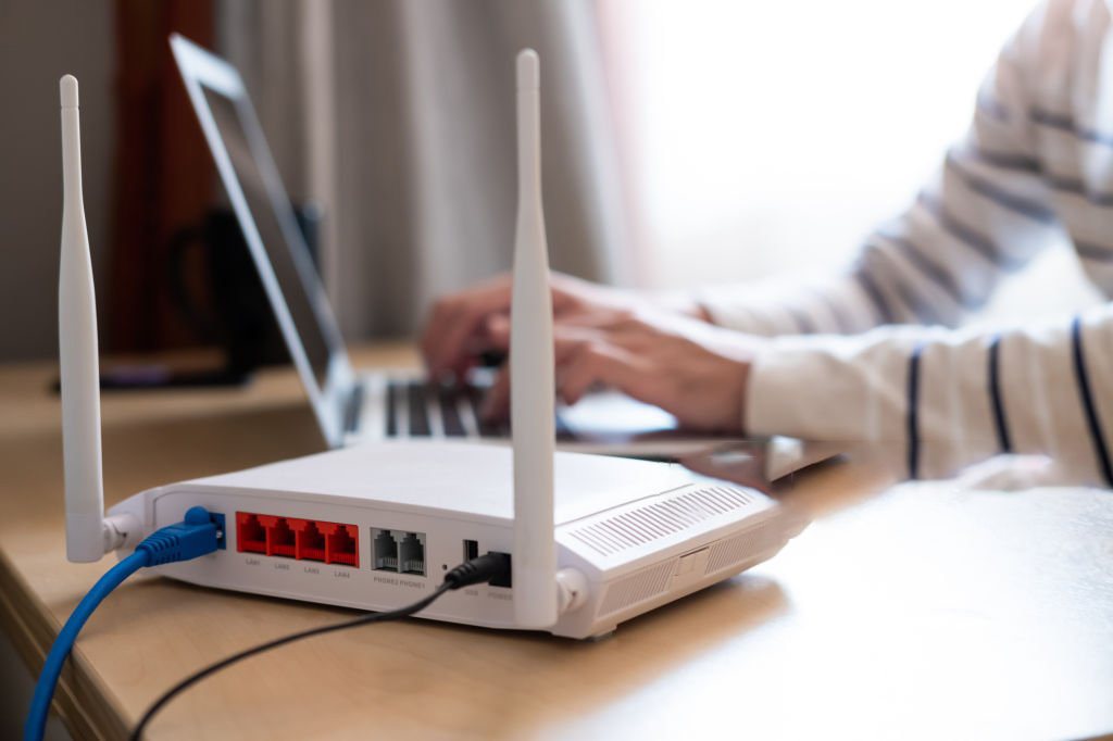 Selective focus at router. Internet router on working table with blurred man connect the cable at the background. Fast and high speed internet connection from fiber line with LAN cable connection.