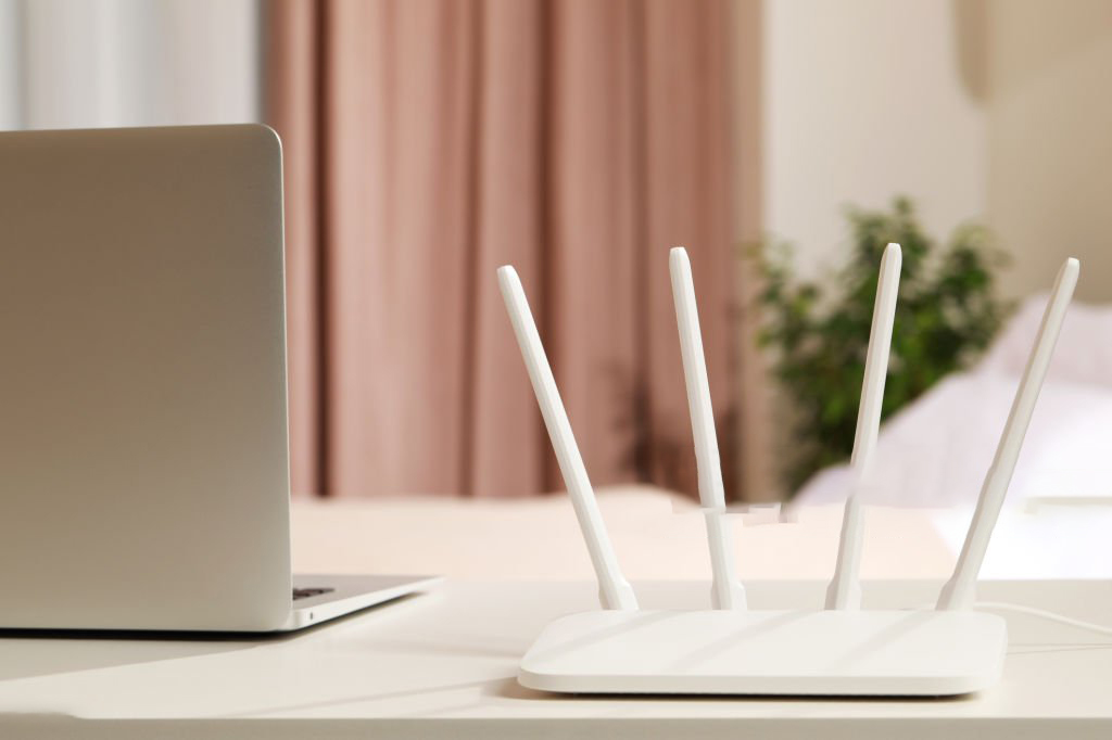 New Wi-Fi router near laptop on white table indoors