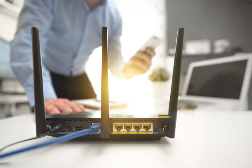 Wireless router with three antennas and cable connected. Man using smartphone in background